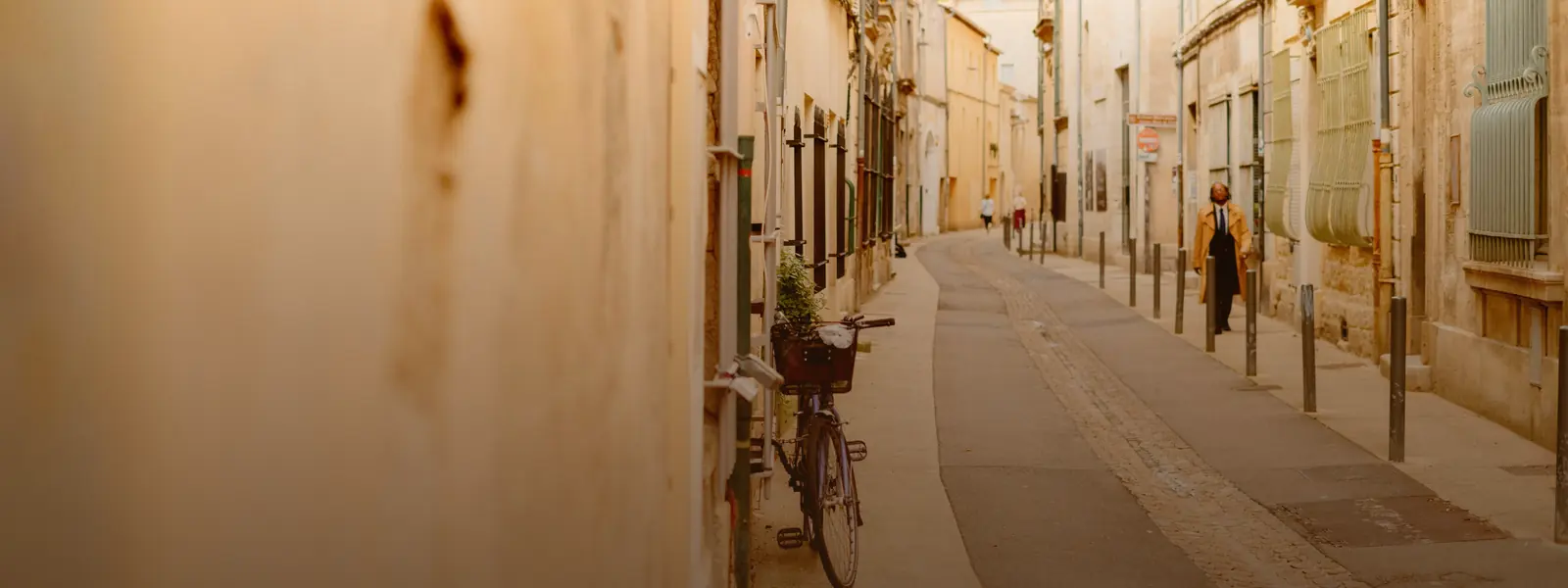 Ruelle étroite d'une vieille ville française, vélo appuyé contre une façade, un passant au fond